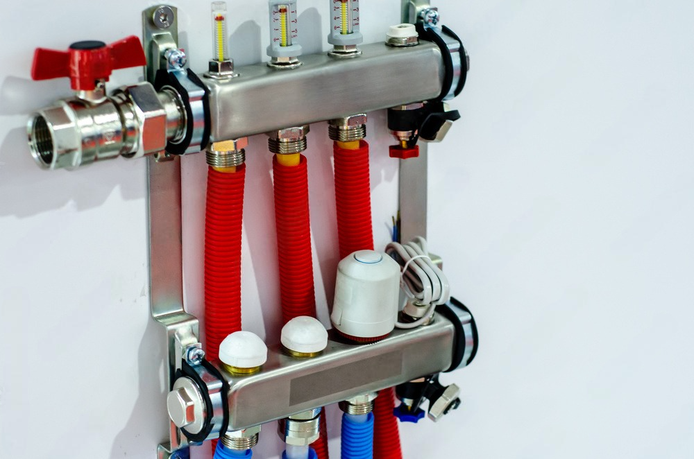 Stainless steel manifold with red and blue tubing for radiant heating, mounted on a white wall.