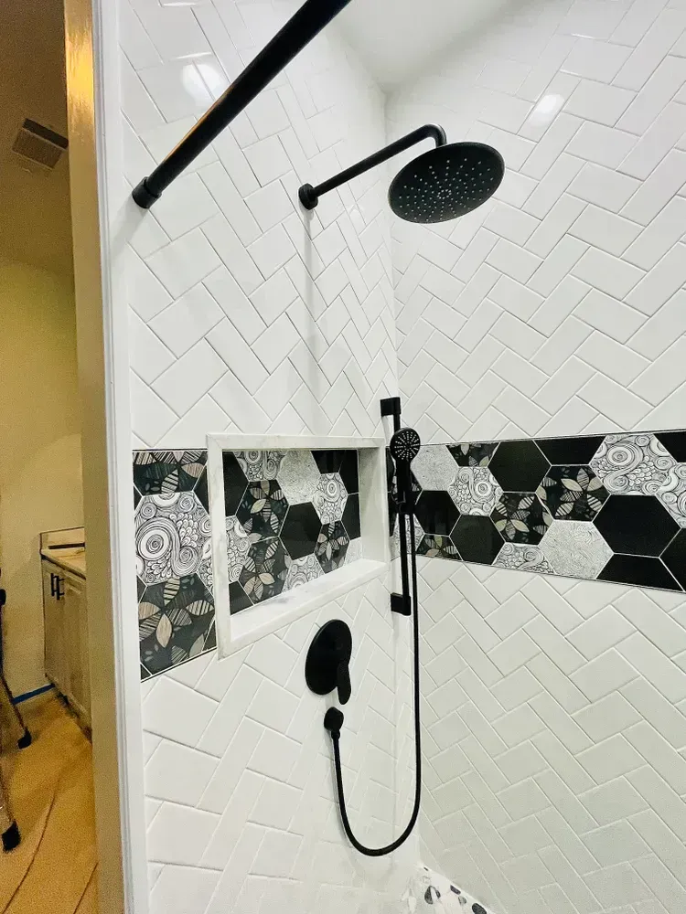 A shower with black and white tiles and a black shower head.