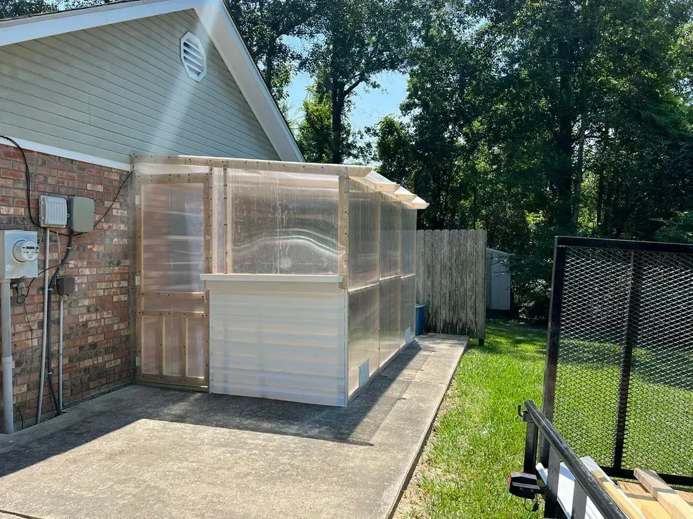 A greenhouse is sitting in the backyard of a house.
