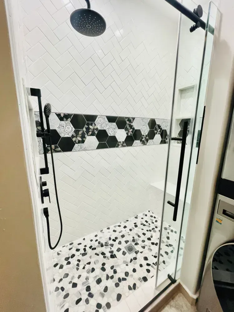 A shower with a black and white tile floor and a shower head.