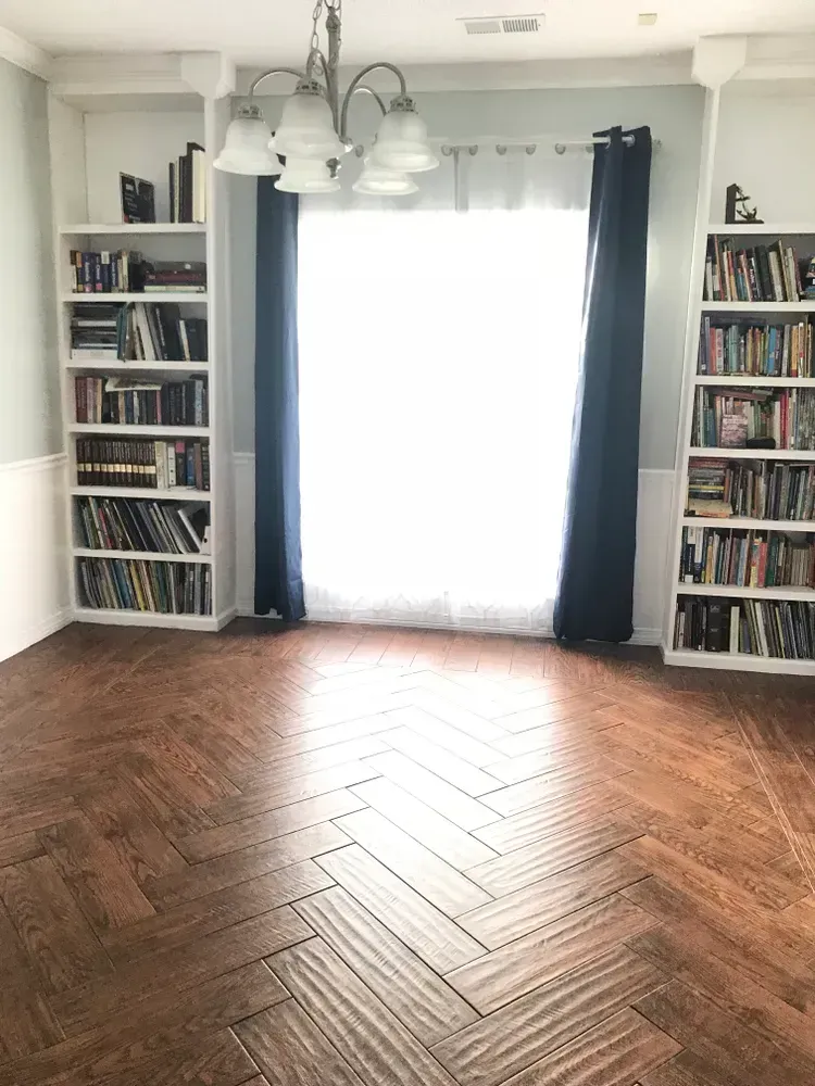 A living room with a herringbone floor , bookshelves , and a chandelier.
