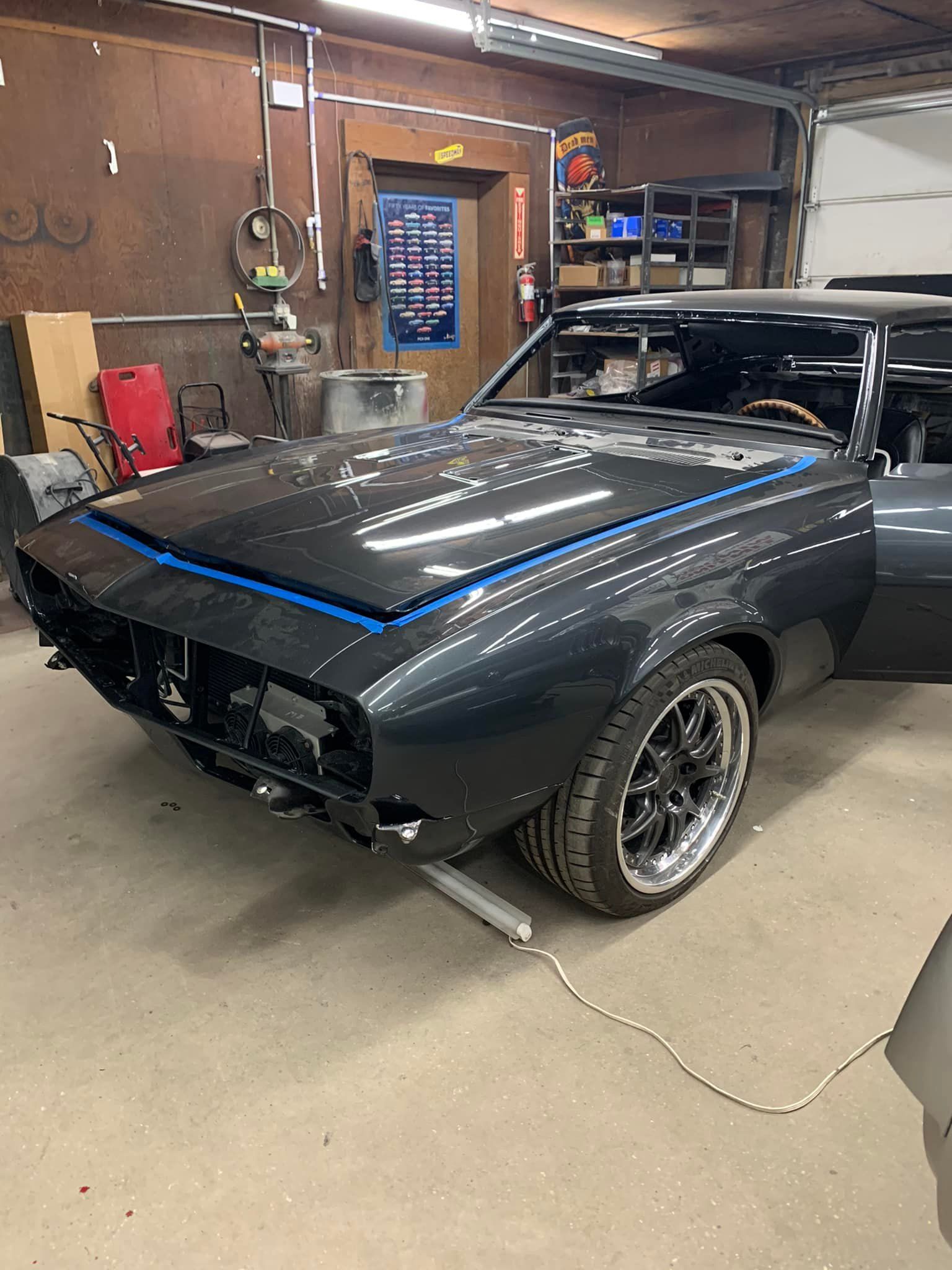 A black car is sitting in a garage with the hood up.