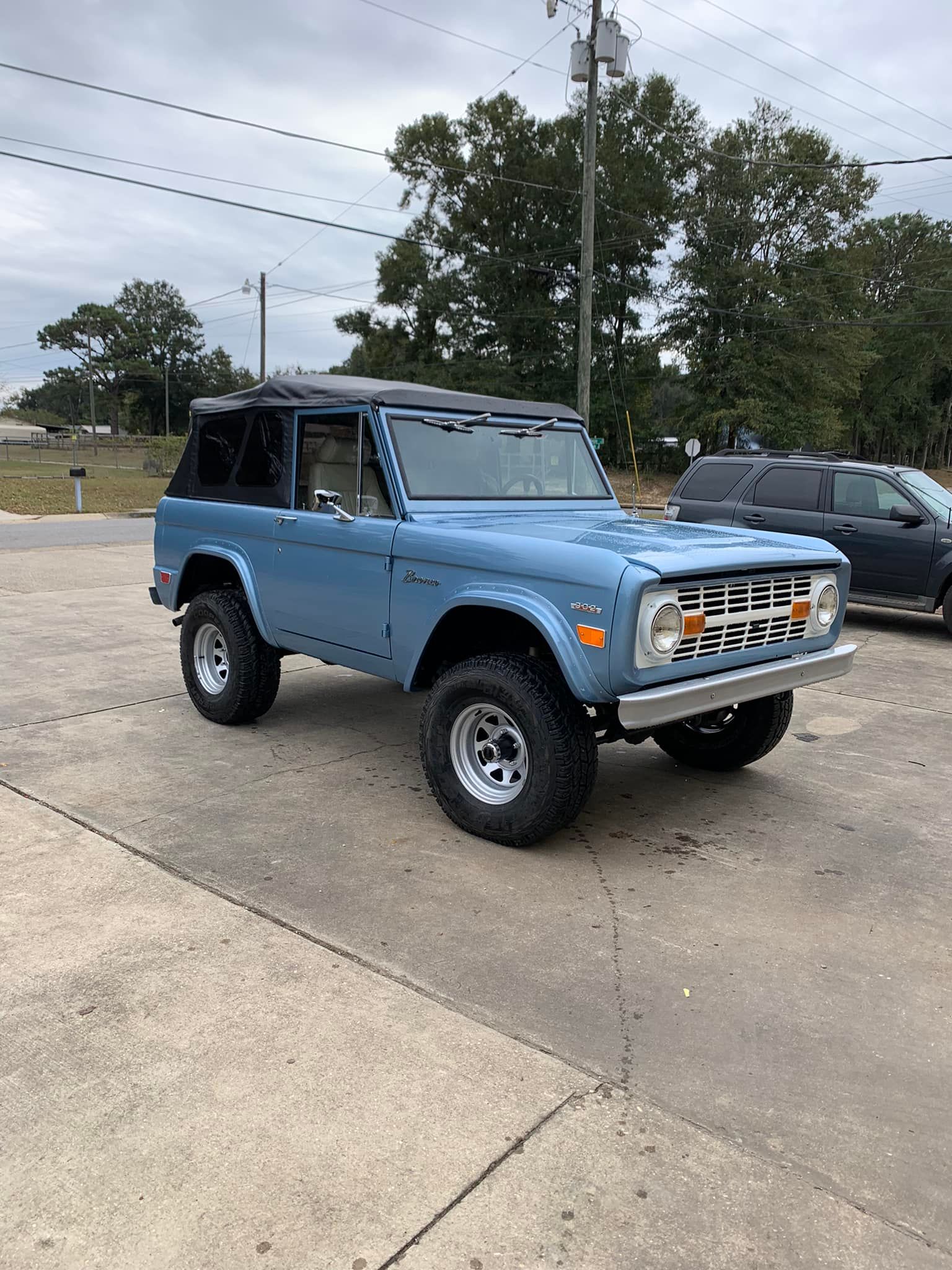 A blue ford bronco is parked in a parking lot.
