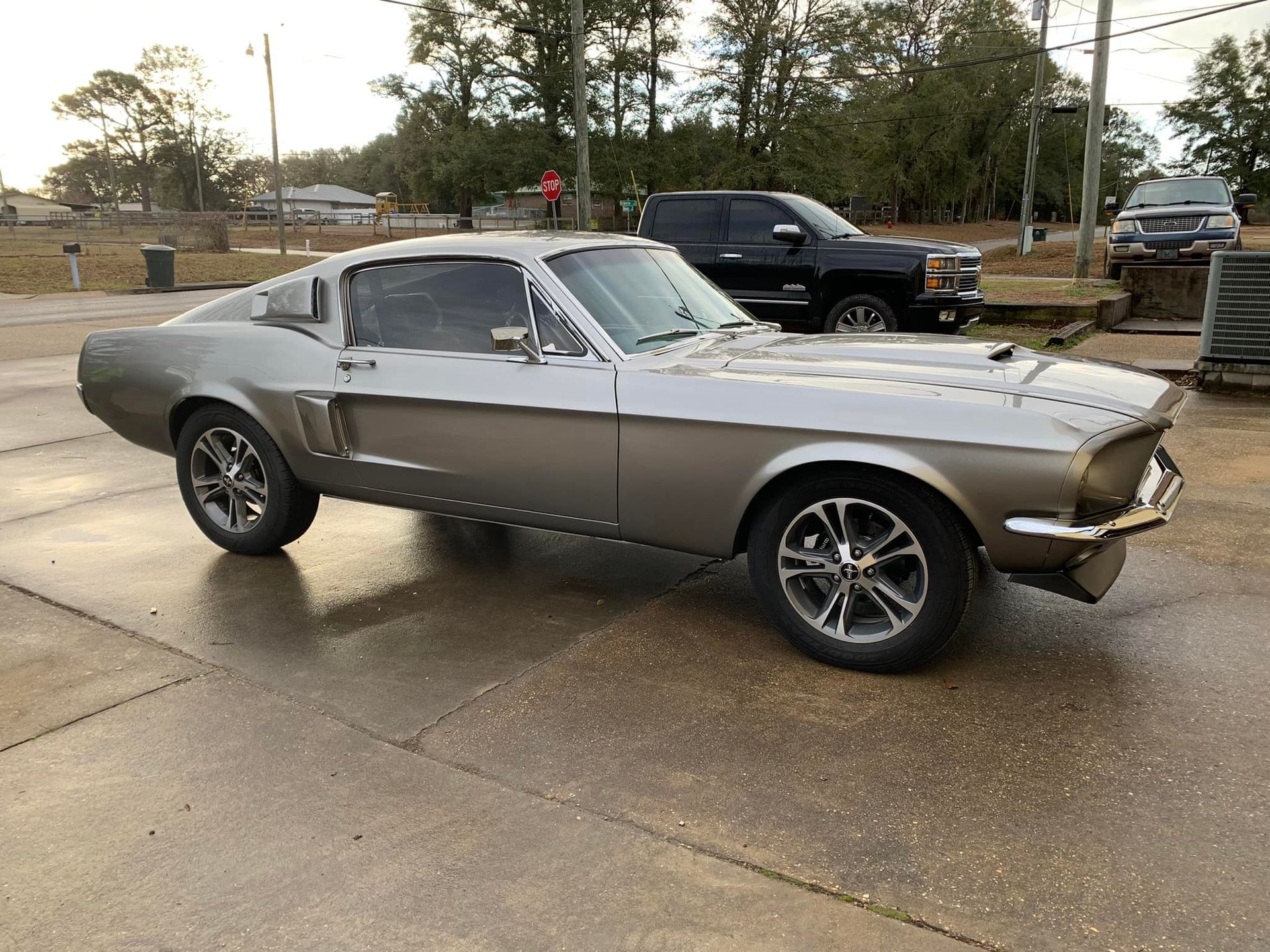 A silver mustang is parked in a parking lot next to a truck.