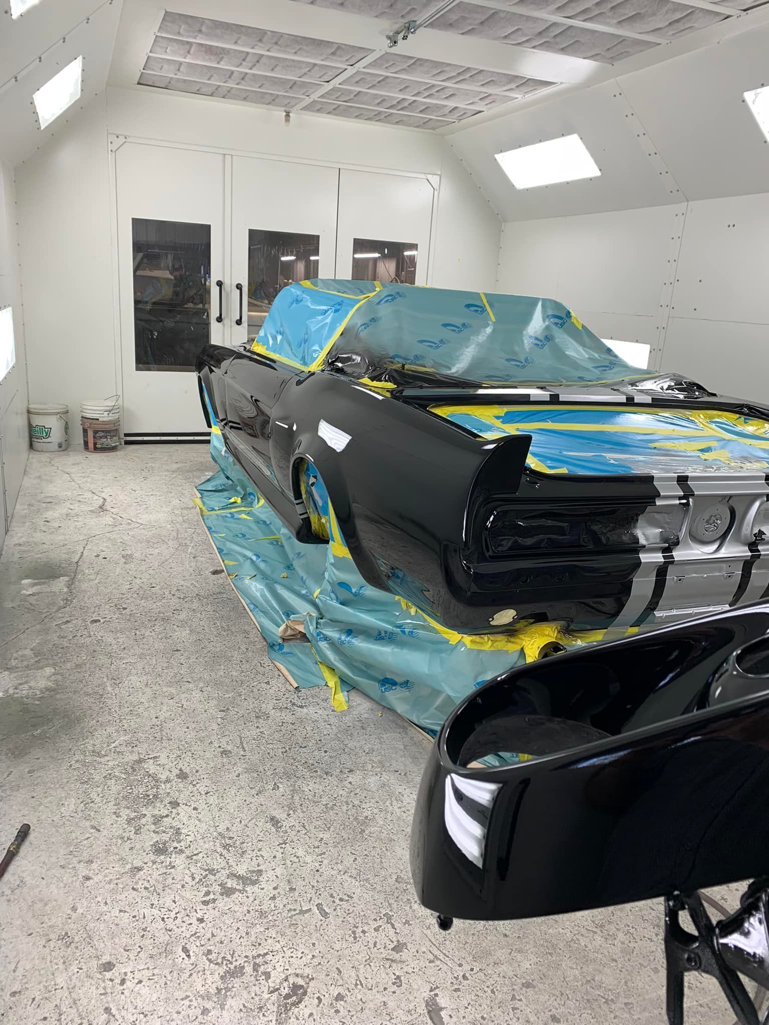 A black car is being painted in a paint booth.