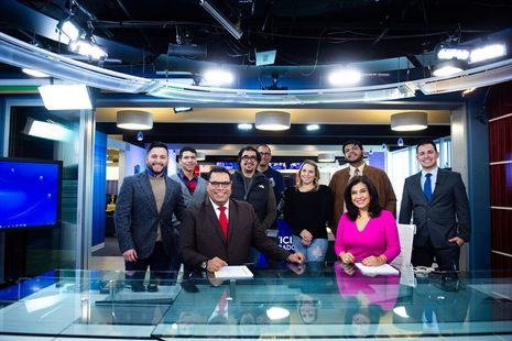 A group of people are posing for a picture in a news studio.