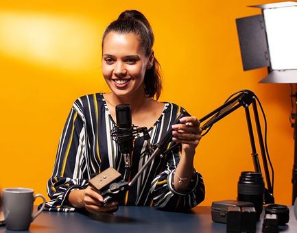 A woman is sitting at a table with a microphone and a camera.