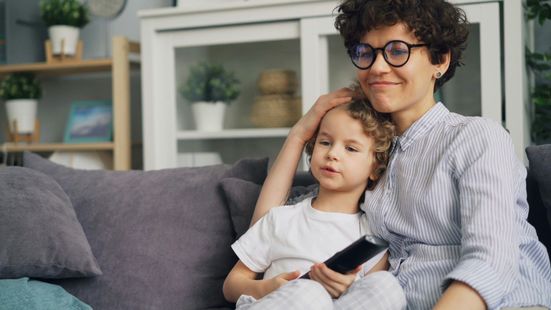 A woman and a child are sitting on a couch watching tv.