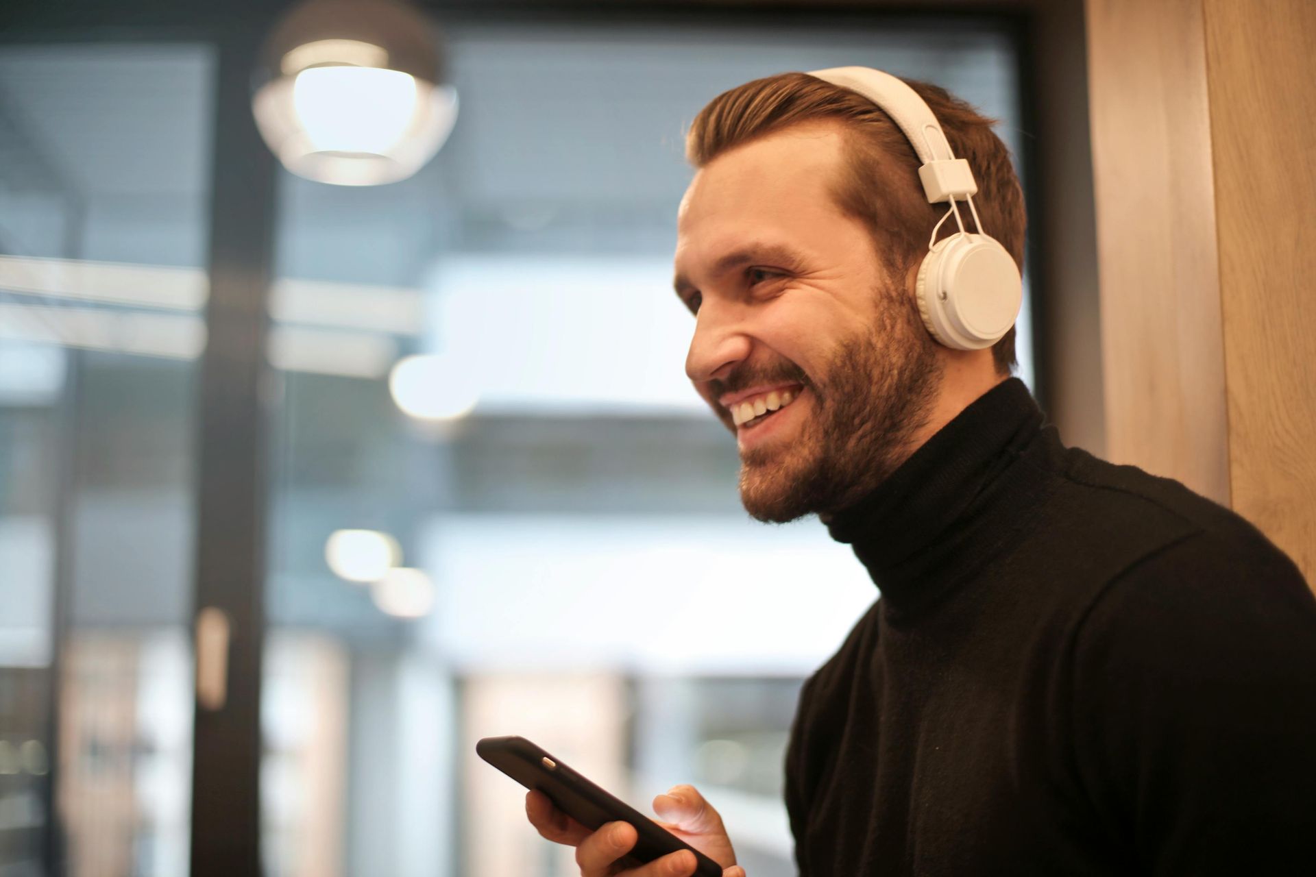 A man wearing headphones is smiling while holding a cell phone.