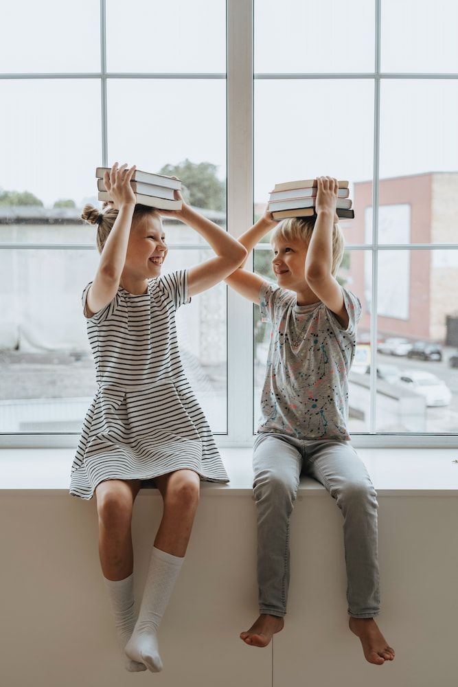 Two Little Girls Are Sitting And Holding Books Over Their Head — Dr Patrick Meaney In Moss Vale, NSW