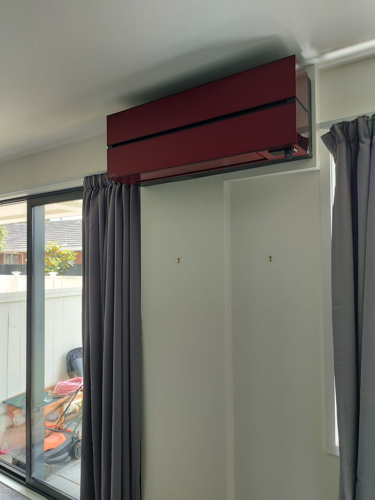 Red air conditioning unit mounted above a wall, flanked by gray curtains and a sliding door.