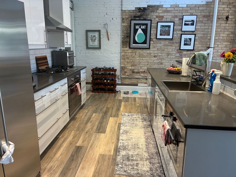 Kitchen with brick wall, stainless steel appliances, cabinets, wine rack, and rug.