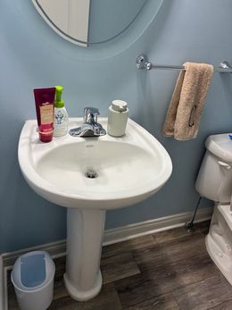 Pedestal sink with toiletries, towel, and trash can in a bathroom with blue walls.