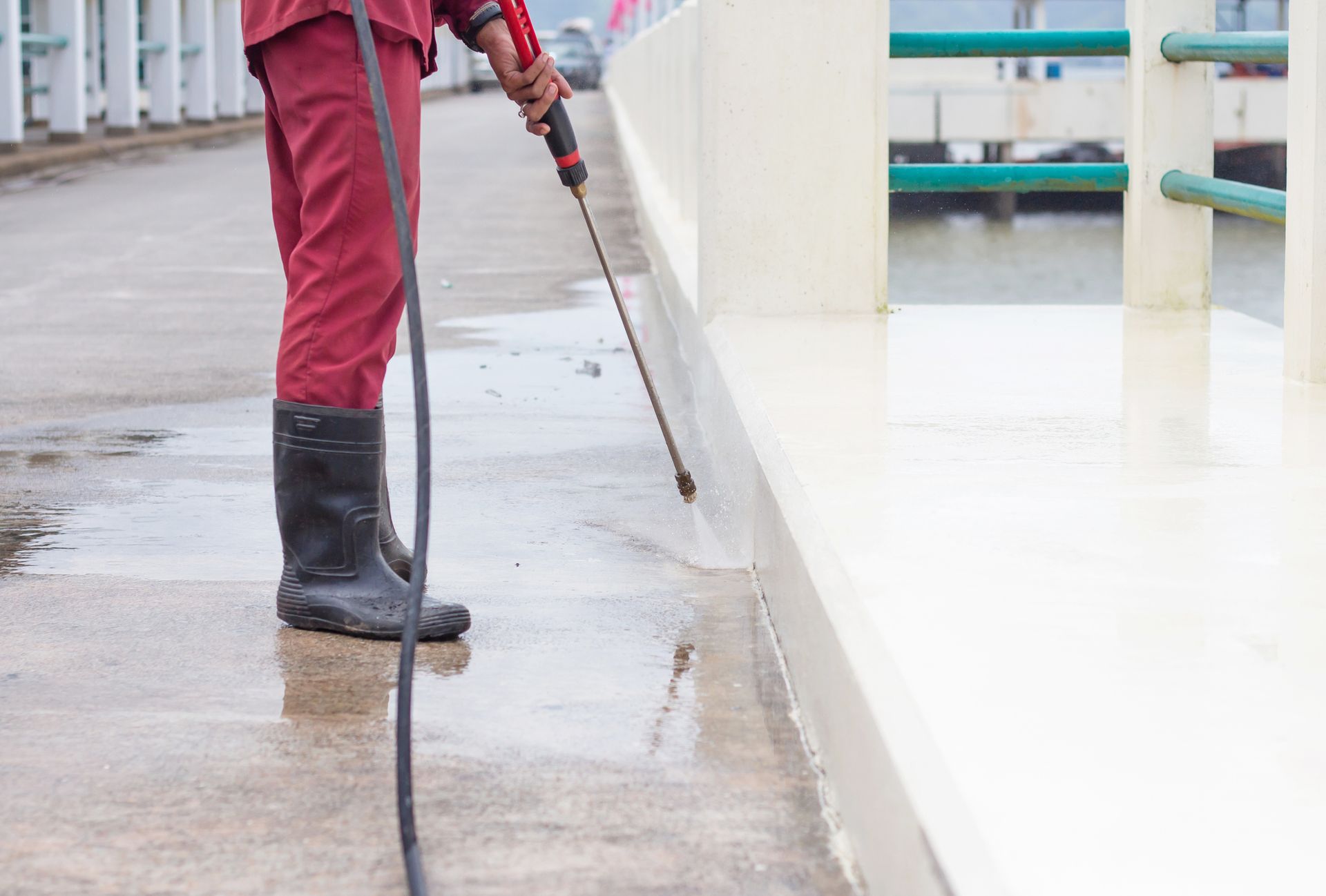 A man is using a high pressure washer to clean a sidewalk.