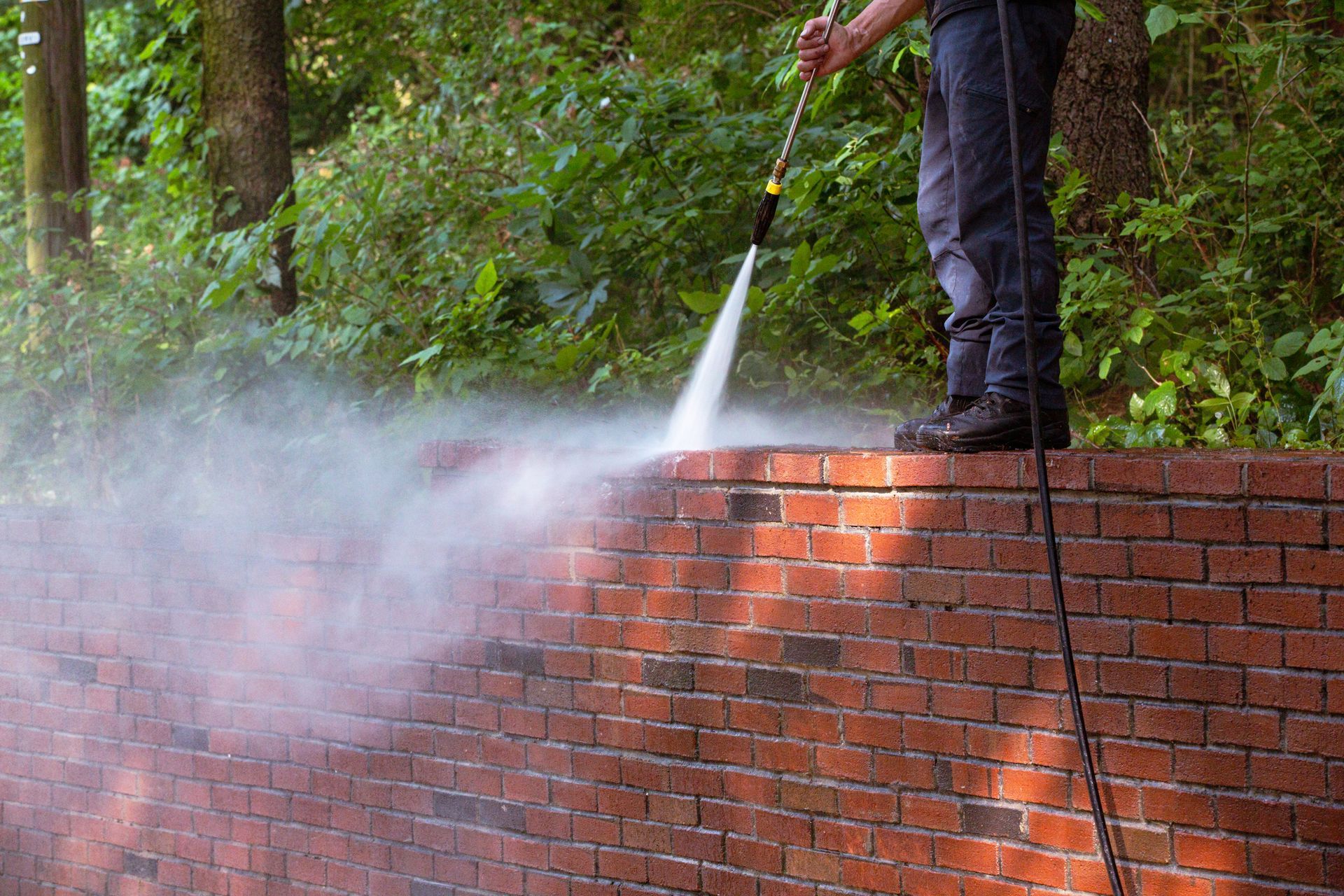 A man is cleaning a brick wall with a high pressure washer.