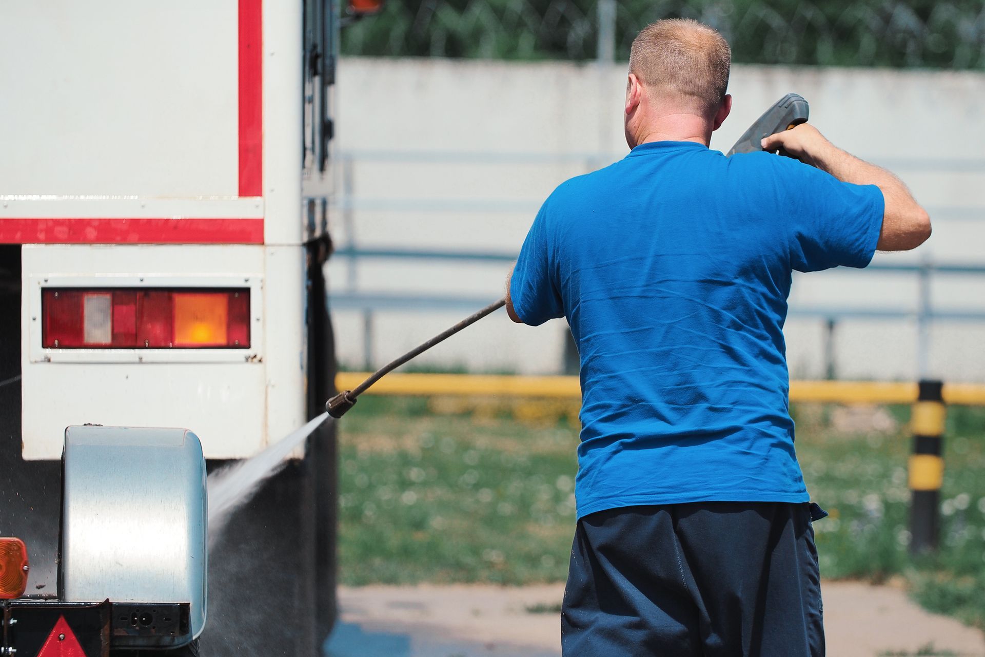 A man is washing a truck with a high pressure washer.