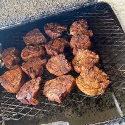 Charred grilled meat pieces on a barbecue grate over ash and embers
