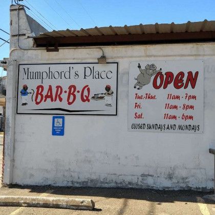 Mumphord’s Place BAR-B-Q storefront sign on a white wall, with hours posted beside it.