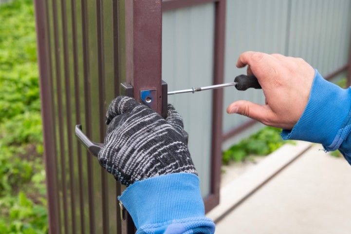 Person tightening a bolt on a metal gate with a screwdriver, wearing gloves.