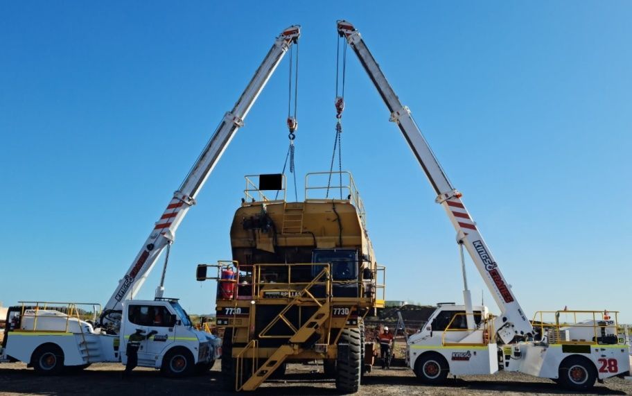 Two Boom Trucks Lifting a Large Green Tank in a Yard Under a Blue Sky — Kings Cranes in Collinsville, QLD
