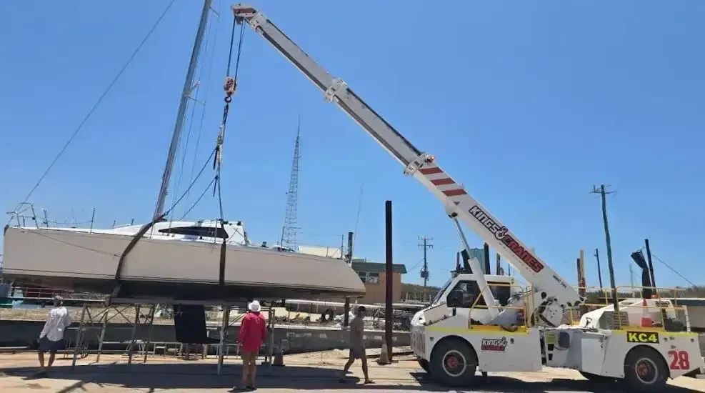 Crane lifting a boat onto a trailer in a sunlit lot with workers nearby under a clear blue sky  — Kings Cranes in Airlie Beach, QLD