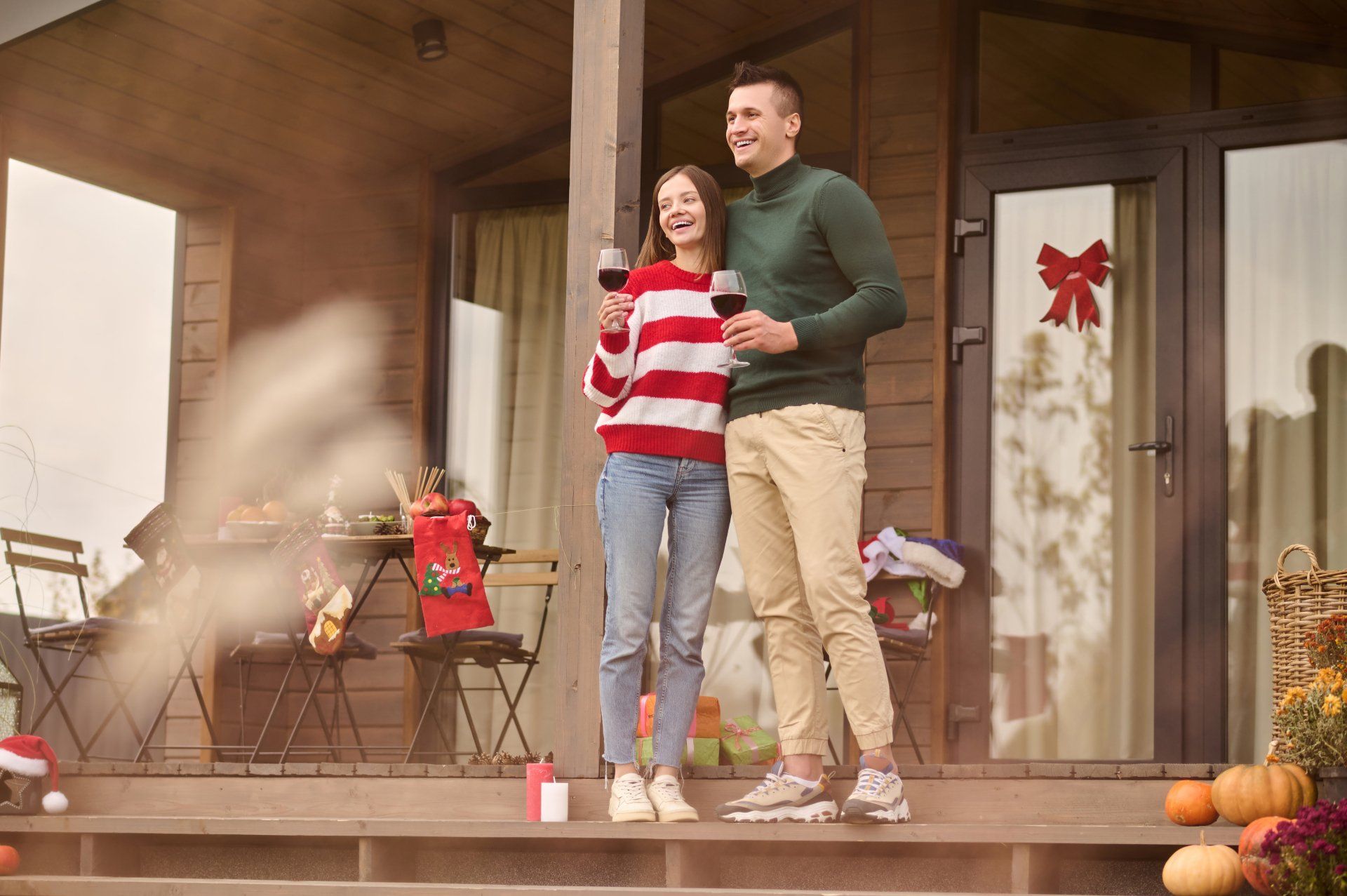 A man and a woman are standing on a porch holding wine glasses.