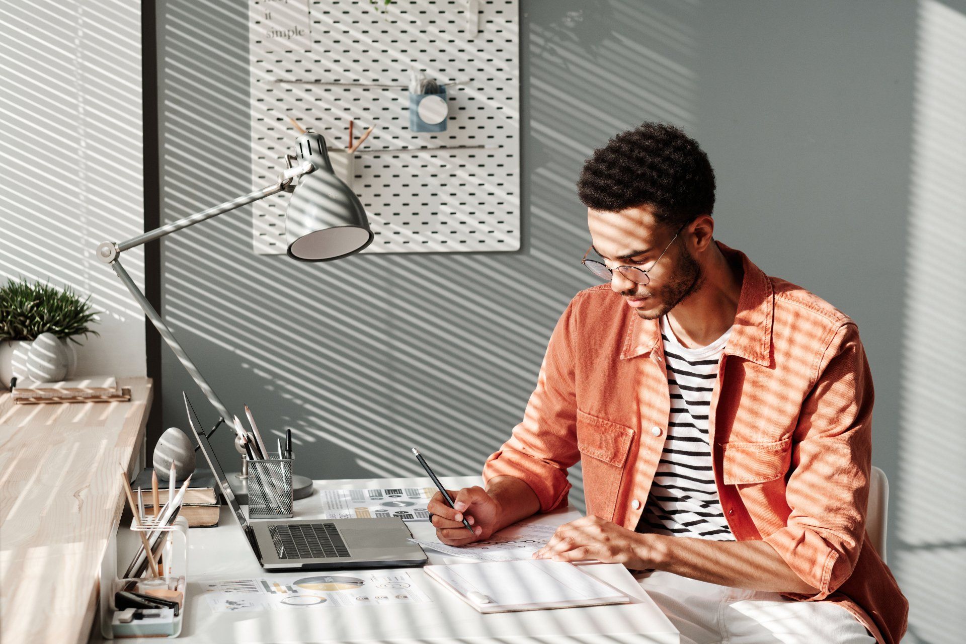 A man is sitting at a desk with a laptop and a pen in his hand.