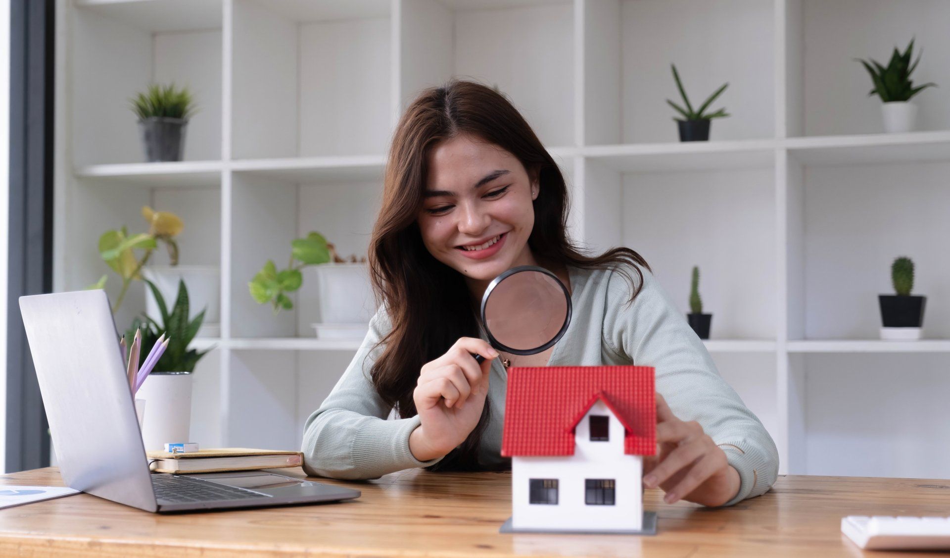 A woman is looking at a model house through a magnifying glass.