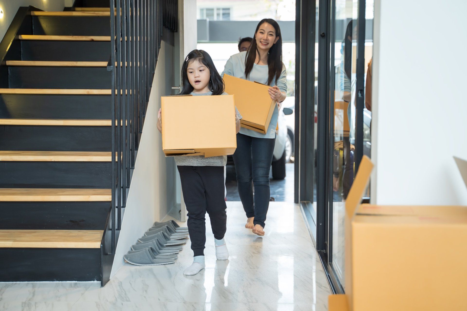 A woman and a child are carrying boxes down a set of stairs.