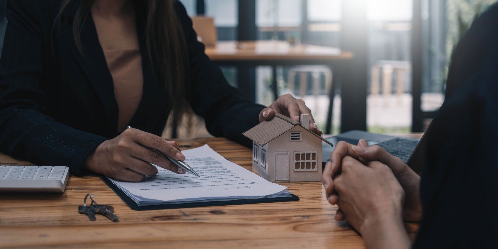 A woman is holding a model house while sitting at a table with a man.