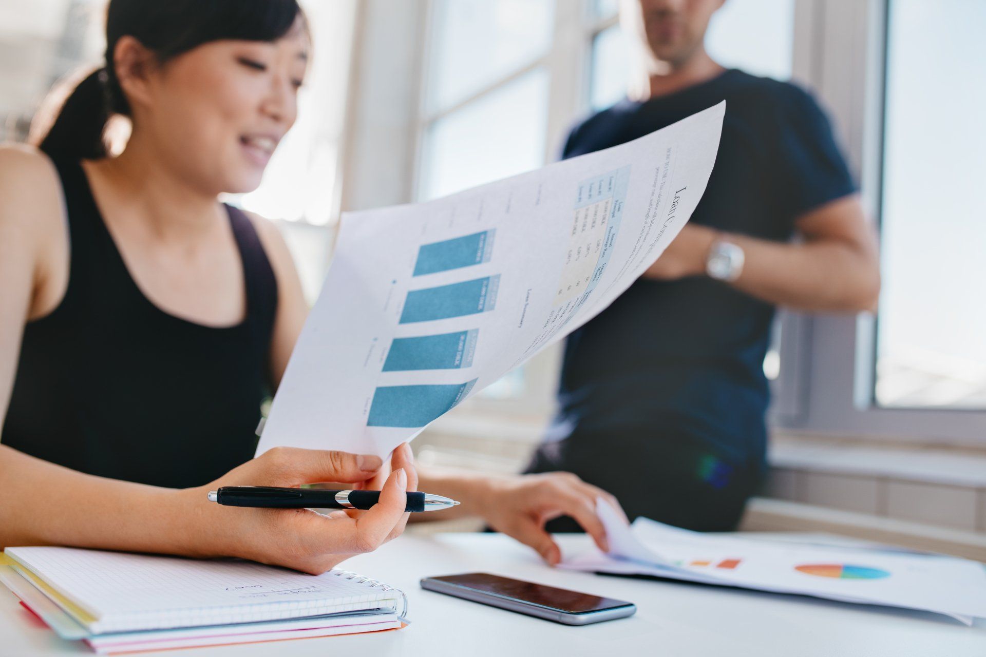 A woman is sitting at a table looking at a piece of paper.
