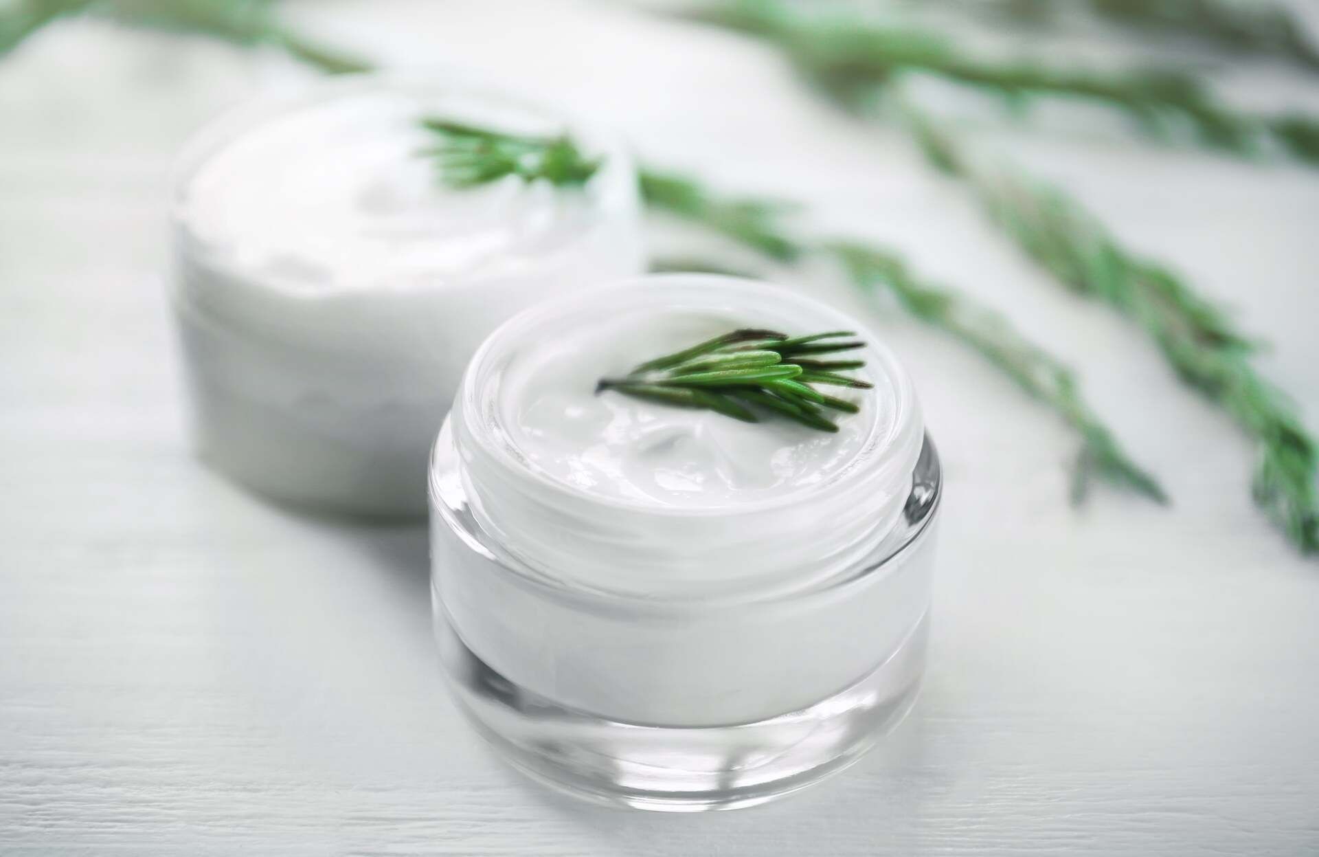 Two Jars of White Cream With Rosemary Sprigs on a White Wooden Surface — Body Sanctuary in Anula, NT