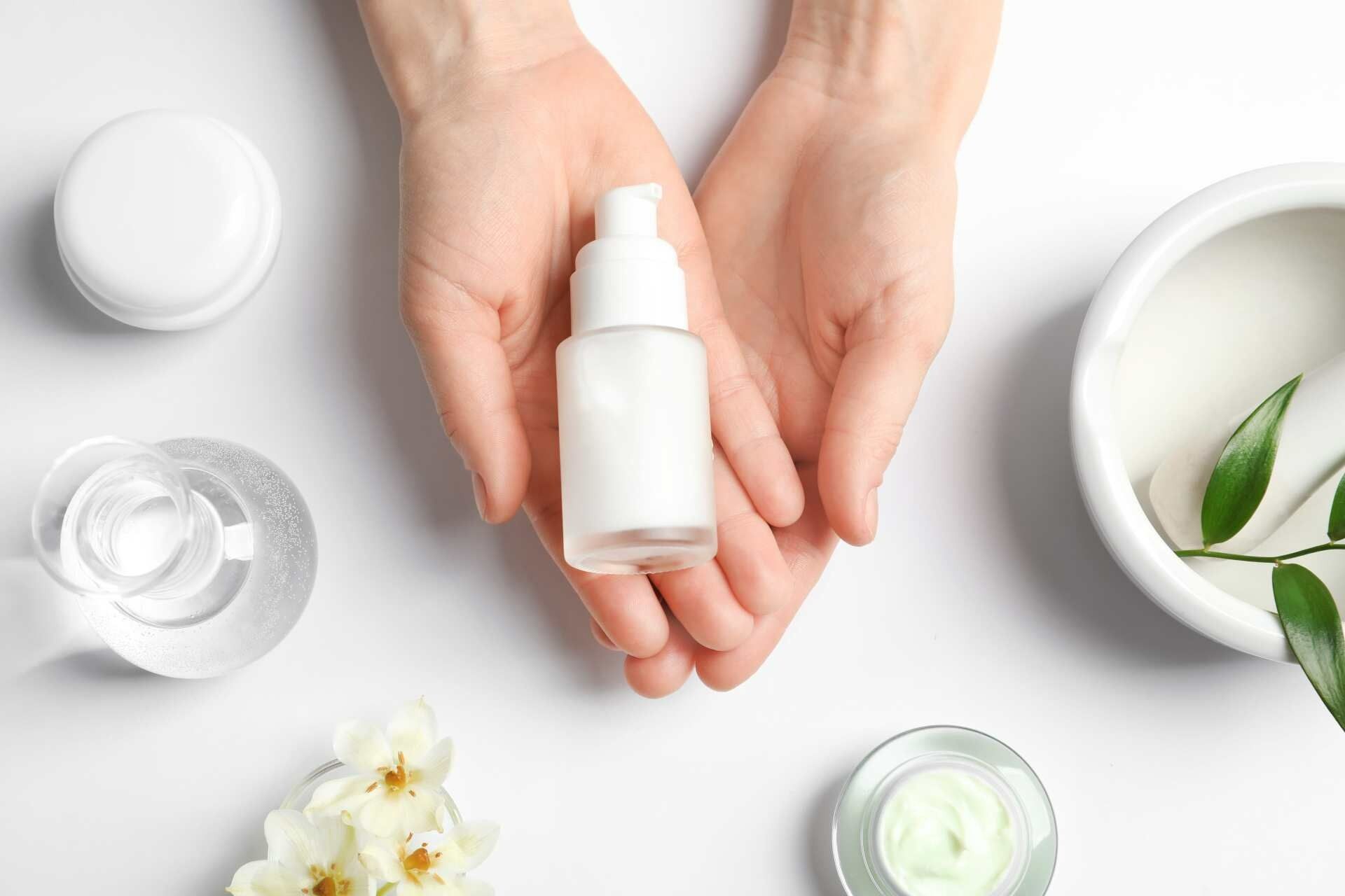 Hands Holding a Skincare Serum Bottle Surrounded by Beauty Products — Body Sanctuary in Anula, NT