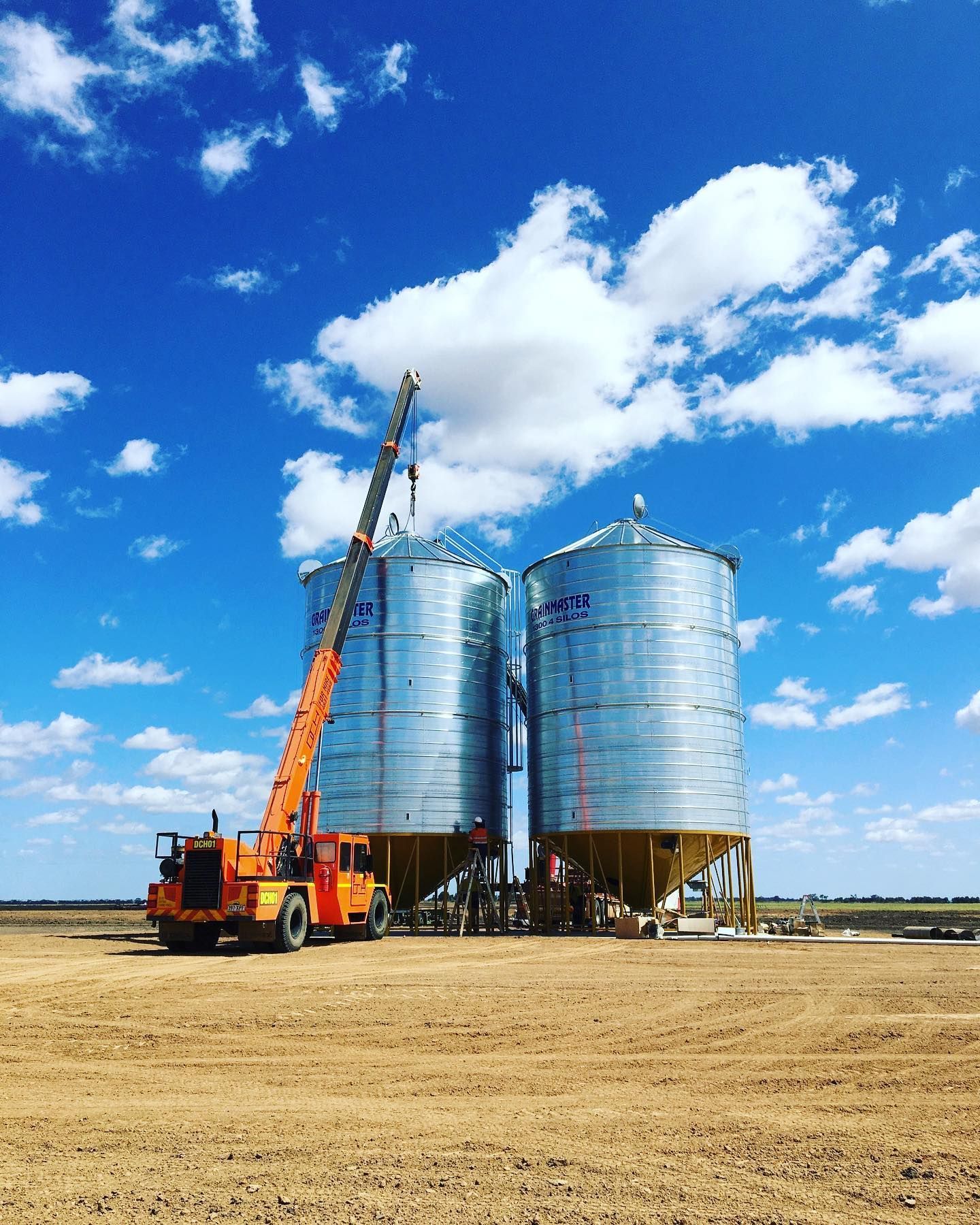 A Crane Is Sitting In Front Of Two Silos In A Field — Dynamic Crane Hire In Emerald, QLD