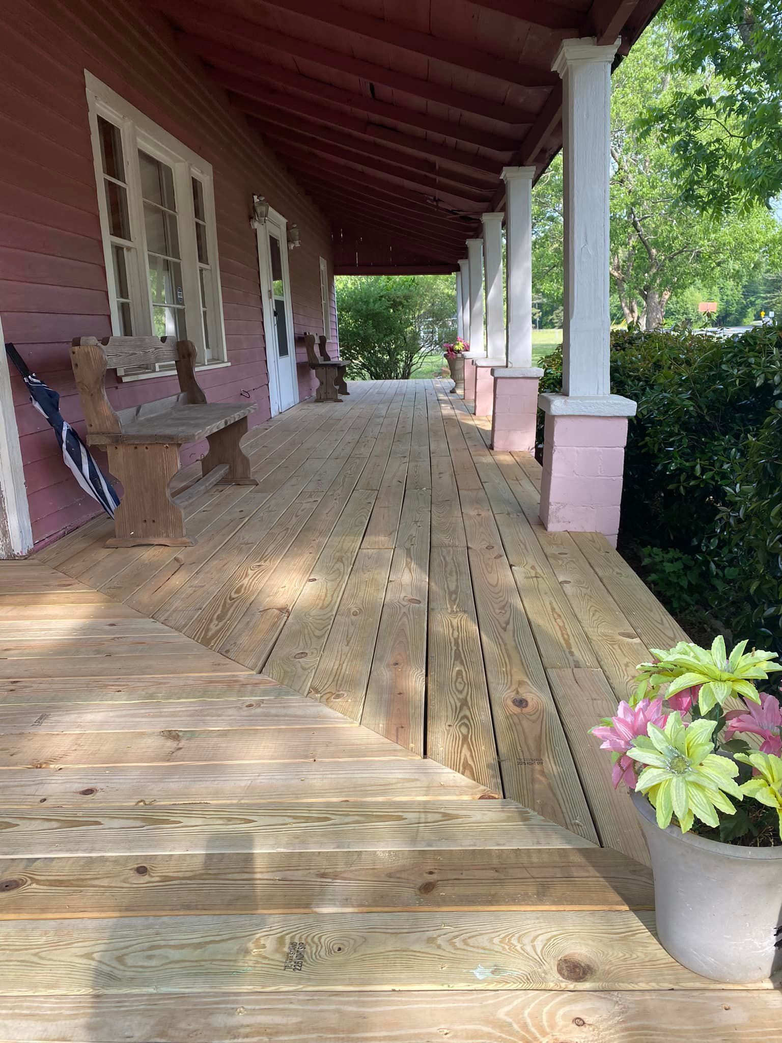 A wooden porch with a bench and a potted plant on it.