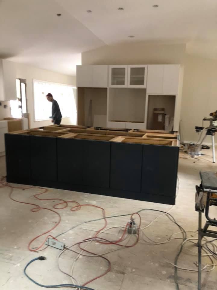 A man is working on a kitchen with a lot of wires on the floor.