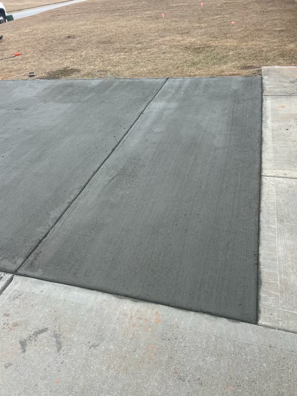 A concrete driveway with a sidewalk and grass in the background.