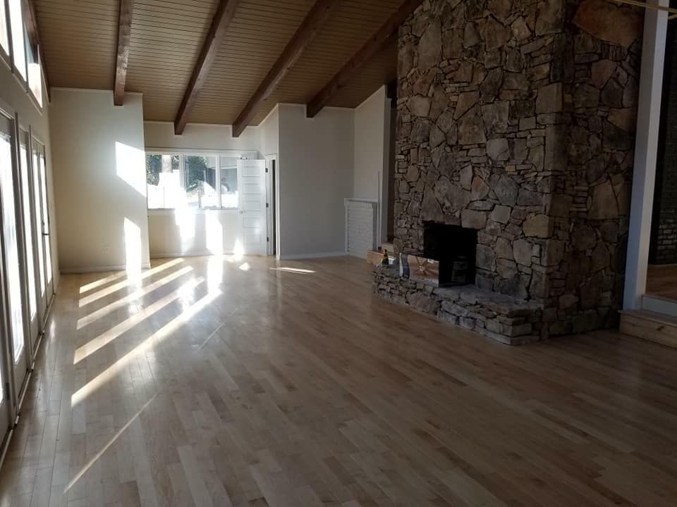 An empty living room with hardwood floors and a stone fireplace.