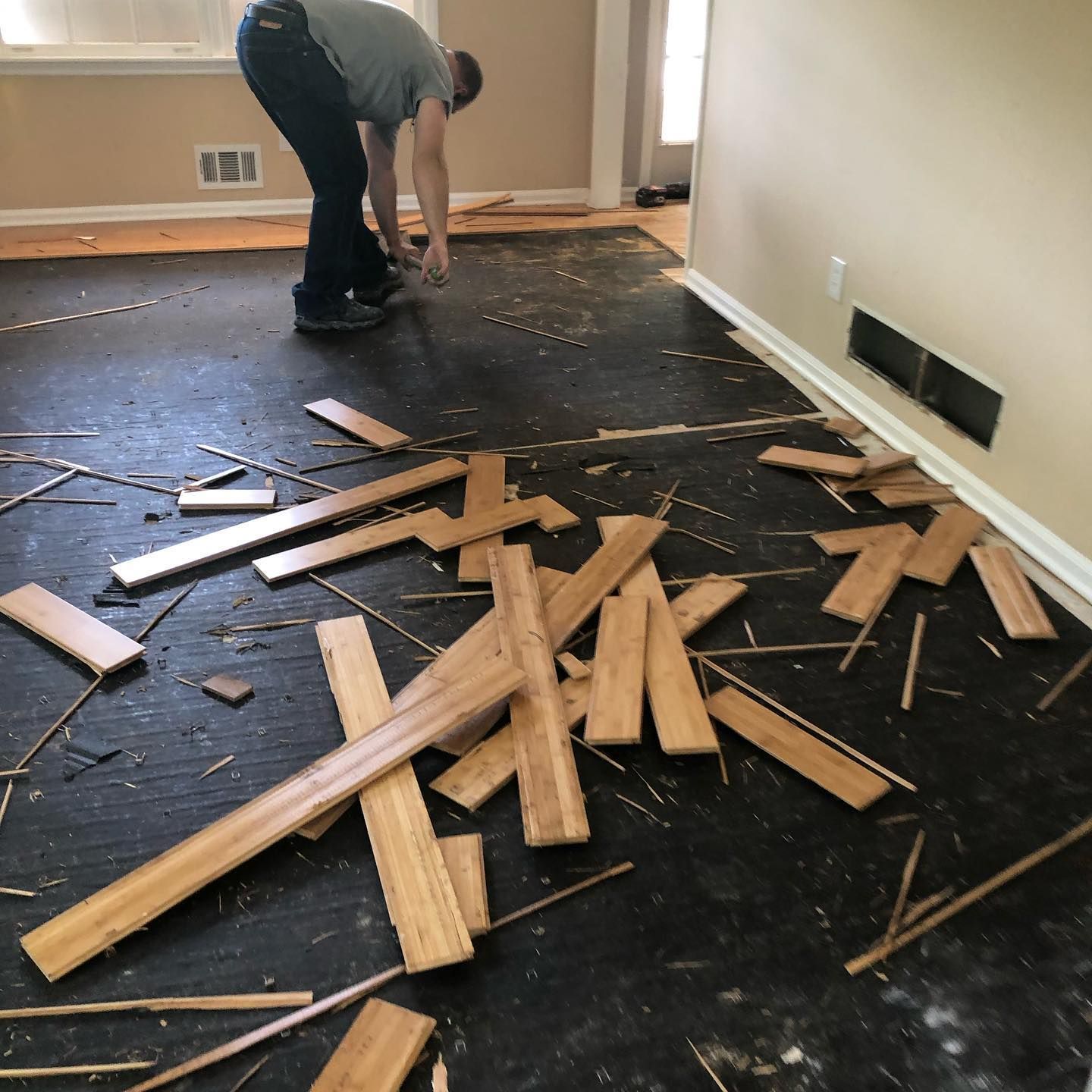 A man is bending over to pick up a piece of wood on the floor