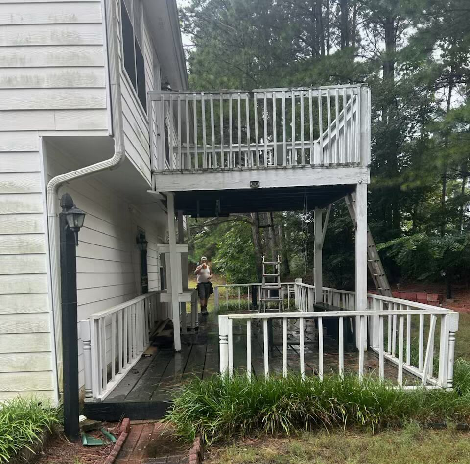 A two-story house with a white deck, brick path, and overgrown yard.