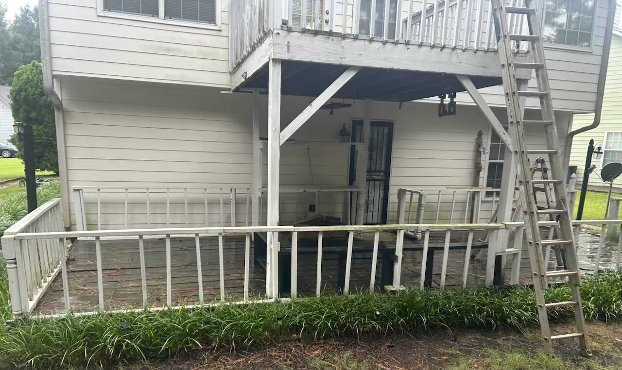 Two-story house with a wooden deck; person stands between levels. Brick pathway leads to the deck from the yard.