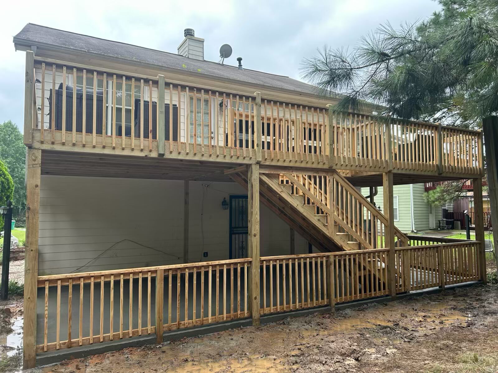 Two-story wooden deck attached to a house, with stairs and railings; outdoors, cloudy.