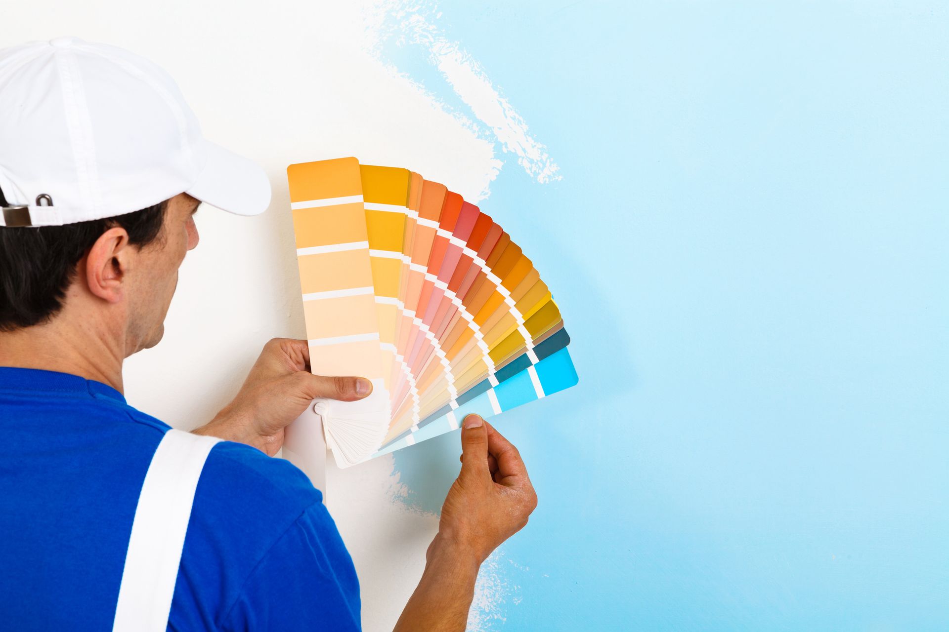 A man is looking at a color palette while painting a wall.