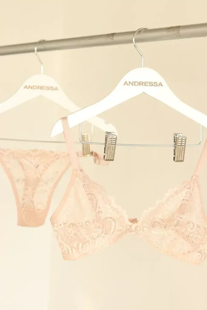 Mujer en lencería blanca posa entre enredaderas verdes.