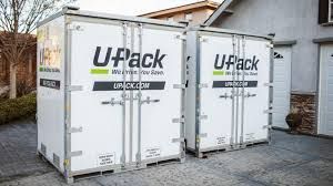 Two white U-Pack storage containers parked on a driveway beside a house.
