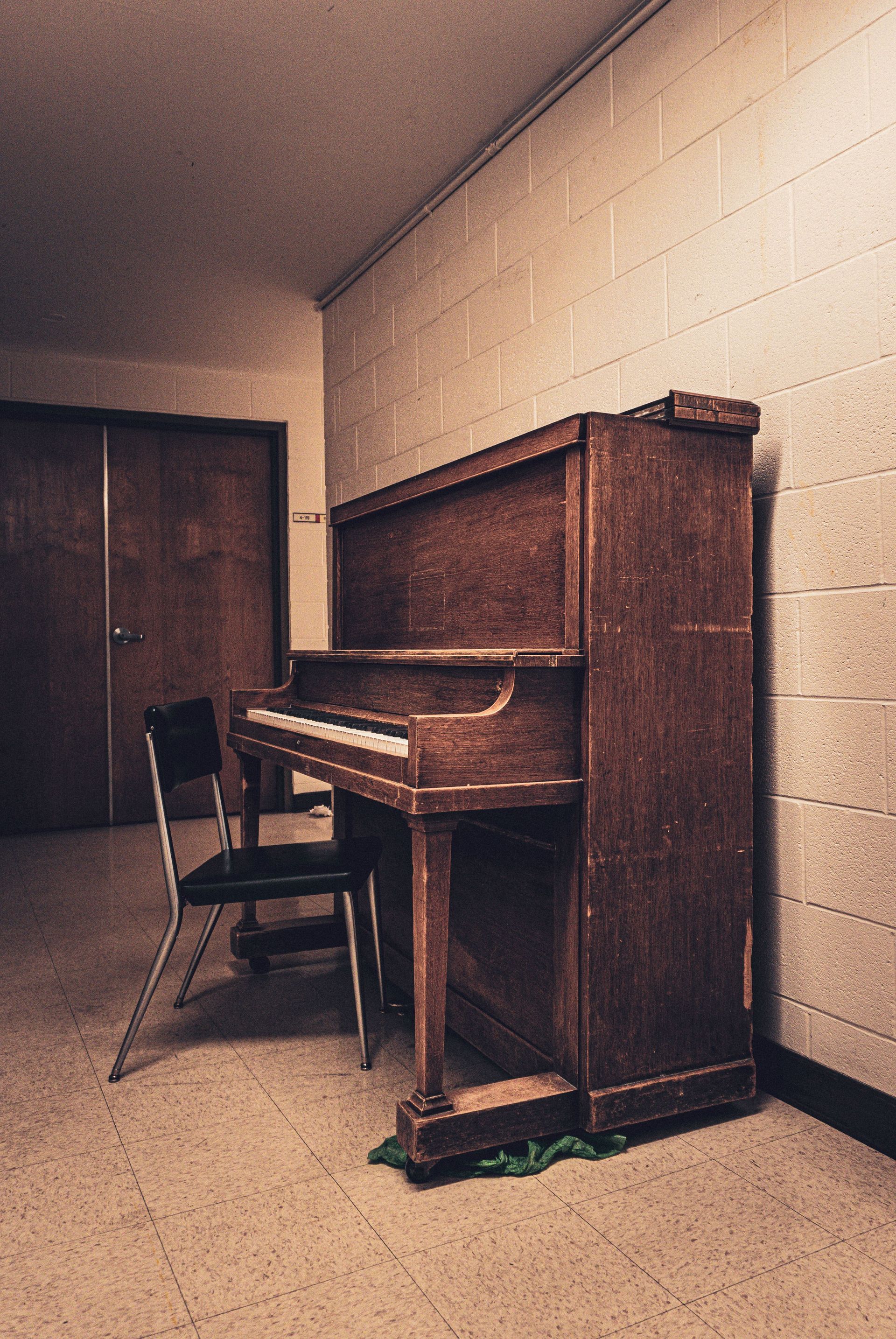 Upright piano in a small beige room beside a chair and closed door