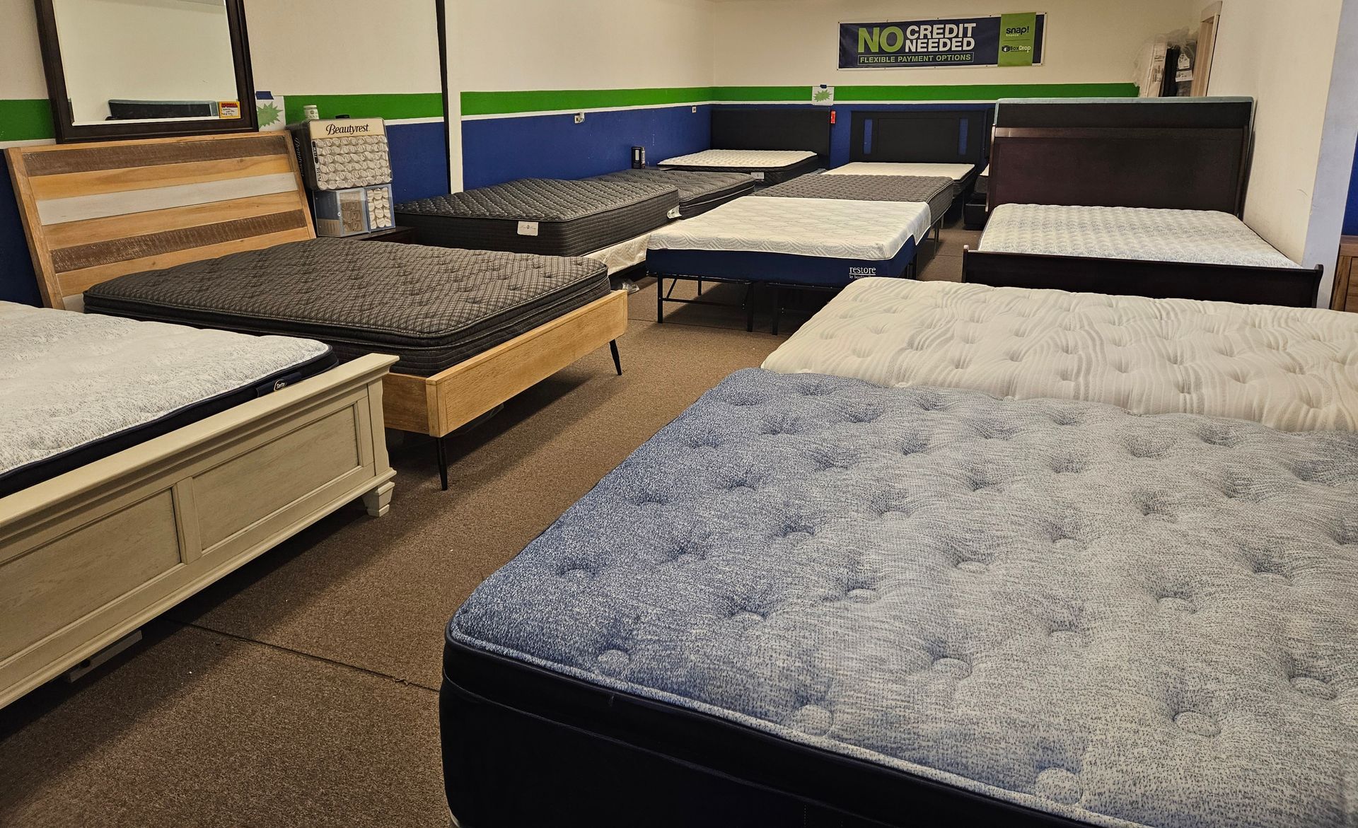 A showroom filled with various mattresses on bed frames, featuring wood, white, and dark blue furniture styles.
