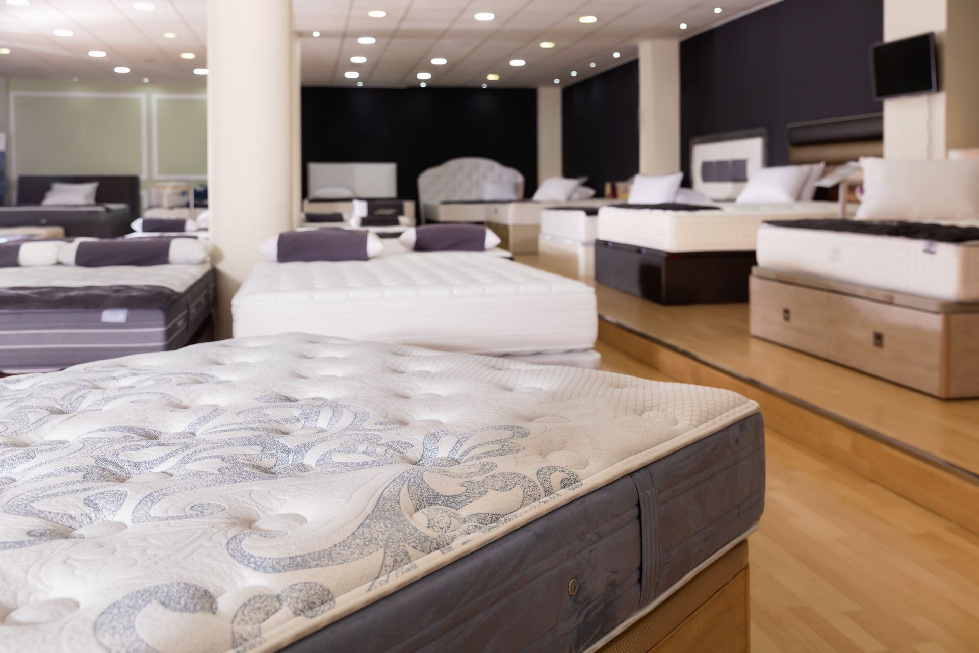 A mattress showroom displaying multiple mattresses arranged in rows on wooden platforms.