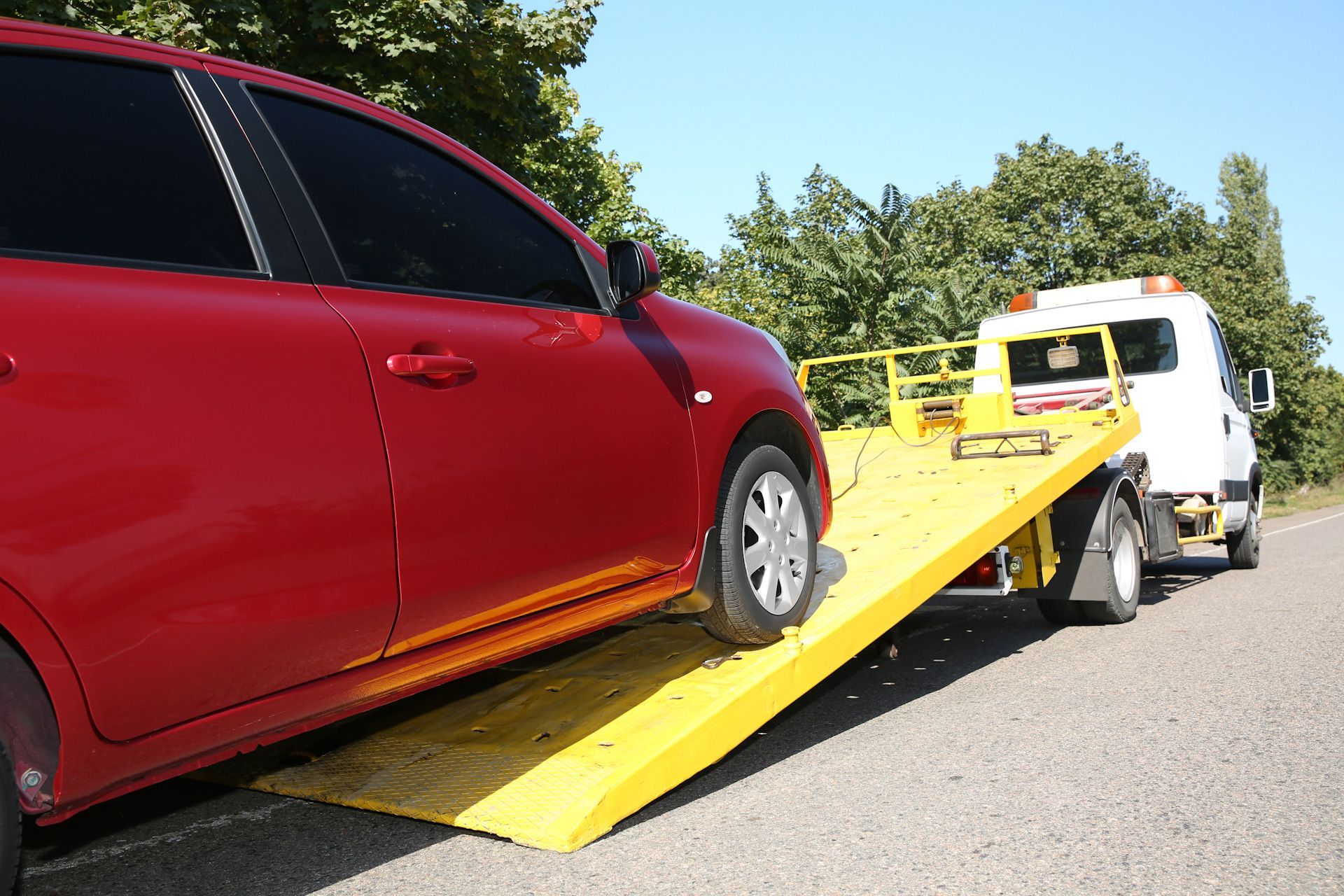 A red car is being towed by a tow truck.
