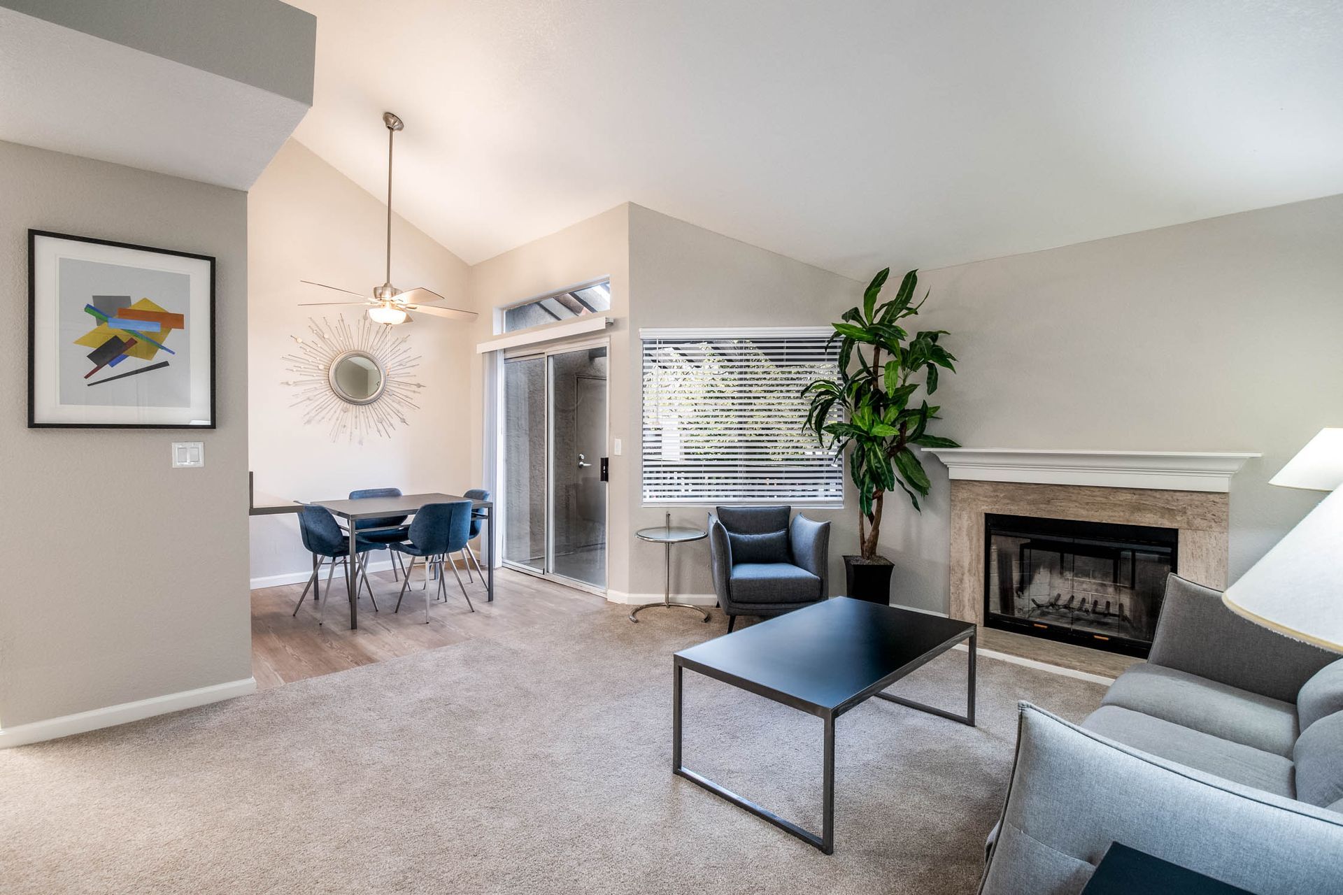 Living room in an apartment with a gray sofa, fireplace, plant, and dining area.